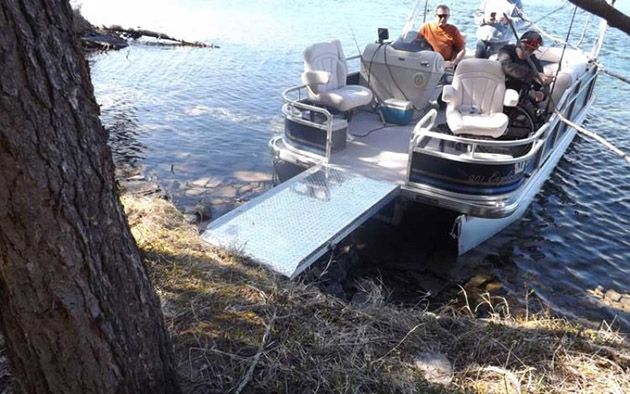 pontoon boat with wheelchair ramp extended pulled up to a grassy shoreline