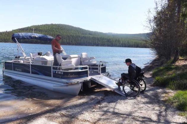 pontoon boat with wheelchair ramp extended onto grassy lake shore line